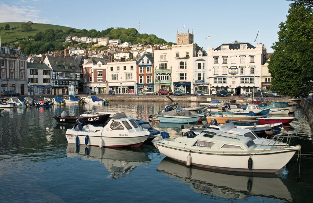 white boats are moored up on the river in Dartmouth, you can see the village in the background