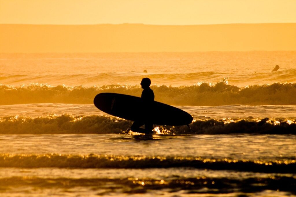image of a man holding surfboard at sunset on a beach