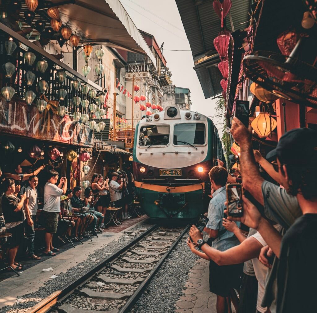 Train on it's way through train street in Hanoi. There are people gathering round to watch and the street is lined with lanterns.